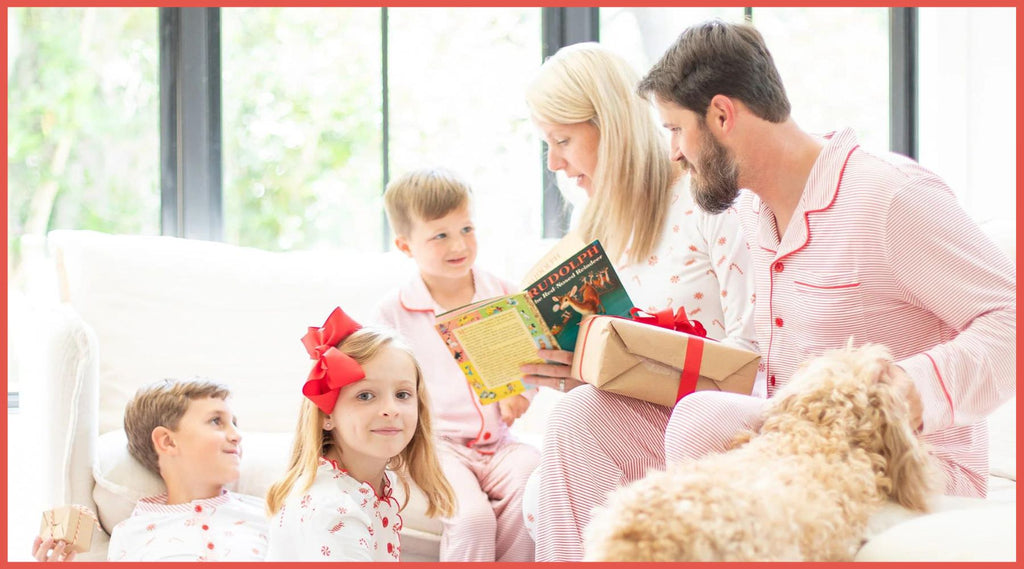 family wearing matching Christmas pajamas reading books with the family dog